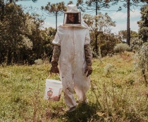 A beekeeper wearing a full heavy cloth beekeeper suit with long cuff gloves.